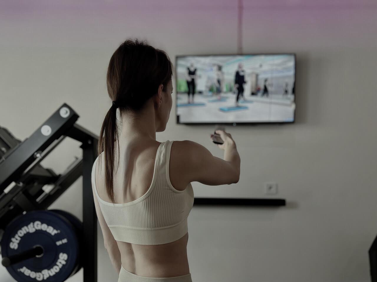 Person in Solospace Gym streaming a workout video on the gym's TV screen, preparing to start their exercise session with gym equipment nearby